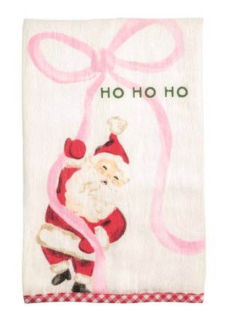 Cream cotton Christmas hand towel featuring a whimsical Santa carrying a large pink bow, "HO HO HO" embroidery, and a red gingham hem.