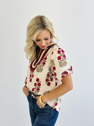 Erin Blouse with pink floral print and accent V-neck collar

Lightweight woven blouse with short bubble sleeves and multicolor trim

Woman wearing Erin Blouse in floral print with band collar detail

Cream floral top featuring vibrant pink flowers and bubble sleeves