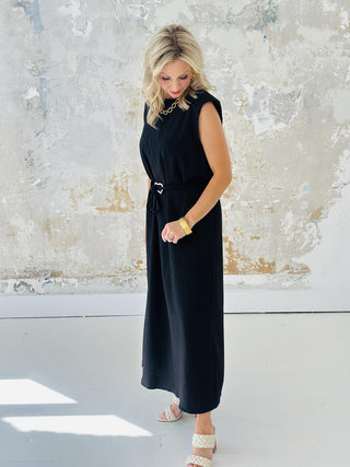 Woman wearing Miley Black Dress, sleeveless black midi dress with gold belt accent

Miley Black Dress with muscle shoulder design and slit hem

Black midi dress with gold embellished belt and back keyhole closure

Elegant sleeveless black dress styled with strappy heels