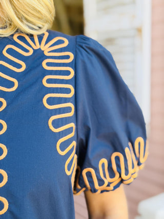 Nora Beth Dress in navy featuring contrasting embroidered trim, puff sleeves, and side pockets.