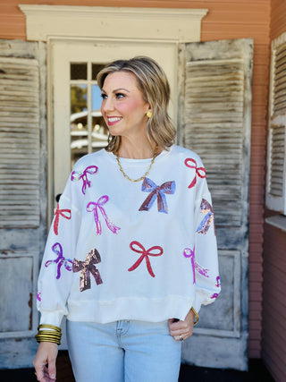 White Lilian Bow Sweater with pink and red sequin bows

Holiday sweater with sparkly sequin bows in pink and red

White festive sweater with multicolor bow embellishments

Lilian Bow Sweater featuring sequin ribbon details

White Christmas bow sweater with shimmering sequin design