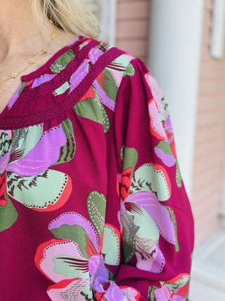 "Janelle Center Stage Plum Top with bold floral print and long sleeves"

"Plum blouse with oversized pink and green floral pattern and ruffle neckline"

"Women’s floral long sleeve top in plum with gathered neckline and relaxed fit"