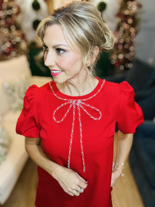 Red short sleeve dress with crystal bow neckline

Claire Dress in red with puff sleeves and rhinestone bow trim

Elegant red A-line holiday dress with crystal bow detail

Red puff sleeve dress with jeweled bow neckline and pockets

Festive red dress perfect for holiday parties and events