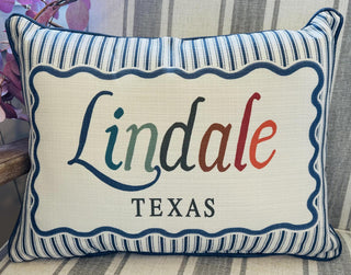 Decorative Lindale, Texas throw pillow with colorful embroidered-style lettering, blue striped border, and navy piping.
