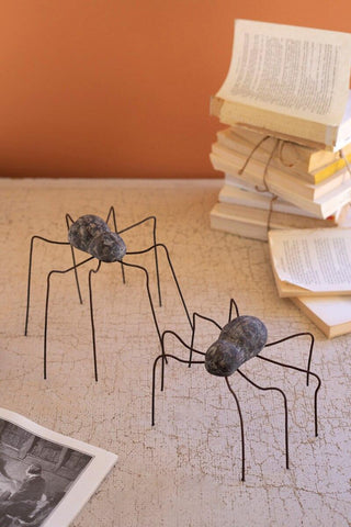 Handmade clay and wire spider sculptures in large and small sizes displayed on a textured tabletop with stacked books.