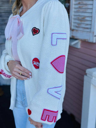 Valentine Patch Cardigan cream knit with red heart patches

Cream cardigan sweater with embroidered hearts and LOVE sleeve

Romantic heart patch cardigan with front tie detail

Cozy cream knit cardigan with red and pink heart accents

Valentine heart cardigan sweater with long sleeves