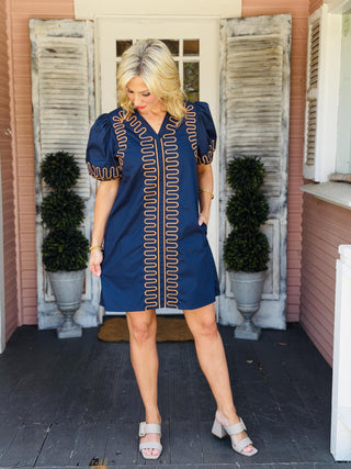 Nora Beth Dress in navy featuring contrasting embroidered trim, puff sleeves, and side pockets.