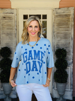 Light blue oversized Game Day graphic short sleeve top with navy polka dots, side slits, and bold varsity-inspired "GAME DAY" lettering.