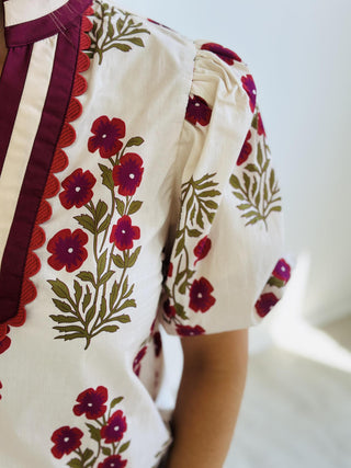 Erin Blouse with pink floral print and accent V-neck collar

Lightweight woven blouse with short bubble sleeves and multicolor trim

Woman wearing Erin Blouse in floral print with band collar detail

Cream floral top featuring vibrant pink flowers and bubble sleeves