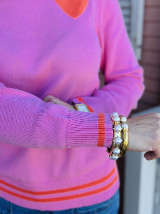  Pink knit sweater with orange heart detail on chest

Maryam Heart Sweater in pink with striped hem and heart graphic

Women’s bright pink sweater with orange heart and stripe accents

Pink heart sweater with ribbed cuffs and contrast hem