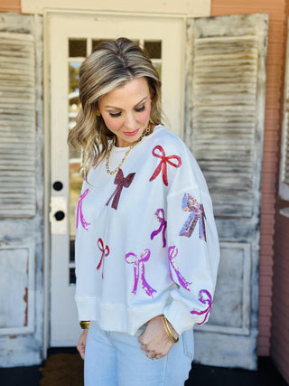 White Lilian Bow Sweater with pink and red sequin bows

Holiday sweater with sparkly sequin bows in pink and red

White festive sweater with multicolor bow embellishments

Lilian Bow Sweater featuring sequin ribbon details

White Christmas bow sweater with shimmering sequin design
