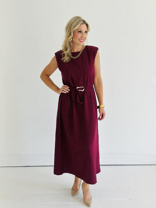 Woman wearing Miley Burgundy Dress, sleeveless burgundy midi dress with gold belt accent

Miley Burgundy Dress with muscle shoulder design and slit hem

Burgundy midi dress with gold embellished belt and back keyhole closure

Elegant sleeveless burgundy dress styled with strappy heels
