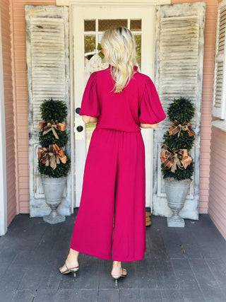 Woman wearing Annalise Berry Jumpsuit with ruffle collar and waist tie

Front view of Annalise Berry Jumpsuit with V-neckline and balloon sleeves

Textured berry jumpsuit with removable waist tie and wide-leg silhouette