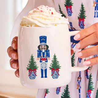 White ceramic mug with blue nutcracker and Christmas tree design

Holiday mug featuring nutcracker and festive greenery

Merry Marchers Christmas mug with blue soldier print

Ceramic nutcracker mug with holiday tree and bow details

Festive coffee mug with blue nutcracker and red ribbon accents