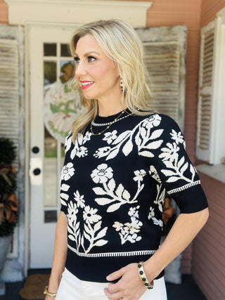 "Black floral sweater top with ivory botanical design, short sleeves, and ribbed trim – Lorelai Sweater Top"

"Lorelai Sweater Top in black with ivory floral print, crew neckline, and cozy sweater knit"

"Women’s floral knit sweater top with bold cream flowers on black background"