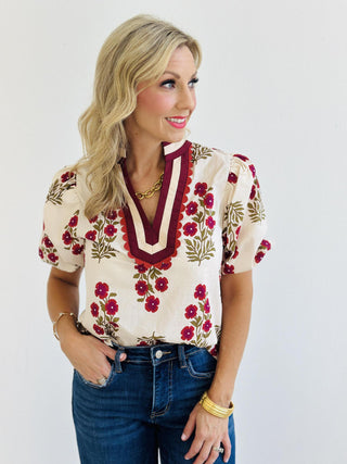 Erin Blouse with pink floral print and accent V-neck collar

Lightweight woven blouse with short bubble sleeves and multicolor trim

Woman wearing Erin Blouse in floral print with band collar detail

Cream floral top featuring vibrant pink flowers and bubble sleeves