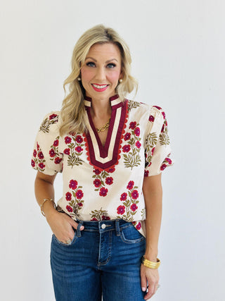 Erin Blouse with pink floral print and accent V-neck collar

Lightweight woven blouse with short bubble sleeves and multicolor trim

Woman wearing Erin Blouse in floral print with band collar detail

Cream floral top featuring vibrant pink flowers and bubble sleeves