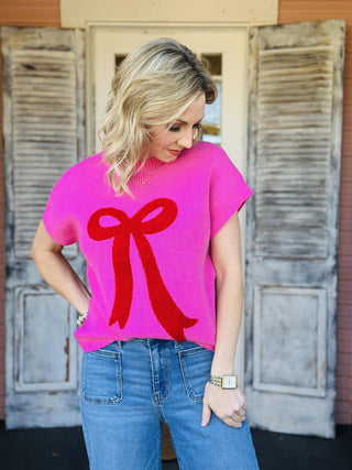 Bright pink knit Lilah Top with red bow detail on front, short sleeves

Women’s pink sweater top with textured red bow design, casual chic style

Close-up of pink knit Lilah Top fabric with raised red bow applique

Short sleeve pink knit top with bold red bow graphic, women’s fashion

Lilah Top pink sweater styled with jeans for everyday wear
