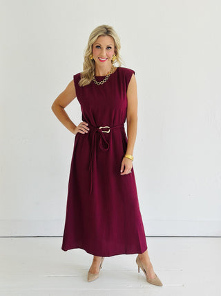 Woman wearing Miley Burgundy Dress, sleeveless burgundy midi dress with gold belt accent

Miley Burgundy Dress with muscle shoulder design and slit hem

Burgundy midi dress with gold embellished belt and back keyhole closure

Elegant sleeveless burgundy dress styled with strappy heels