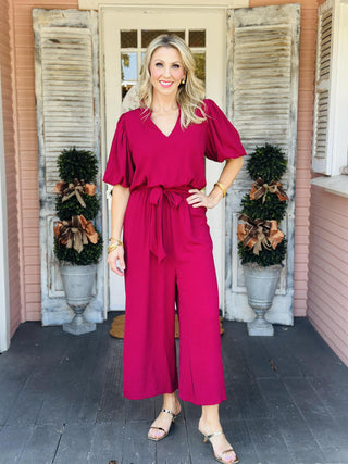Woman wearing Annalise Berry Jumpsuit with ruffle collar and waist tie

Front view of Annalise Berry Jumpsuit with V-neckline and balloon sleeves

Textured berry jumpsuit with removable waist tie and wide-leg silhouette