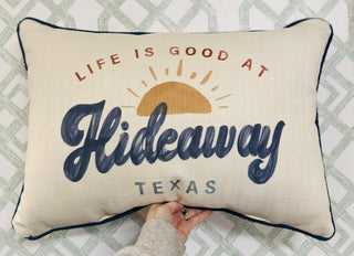 Cream decorative pillow with “Life Is Good at Hideaway Texas” design and sunset graphic.

Hideaway Texas pillow with navy lettering and golden sun illustration.

Rectangular Texas-themed pillow with cheerful sunrise artwork.