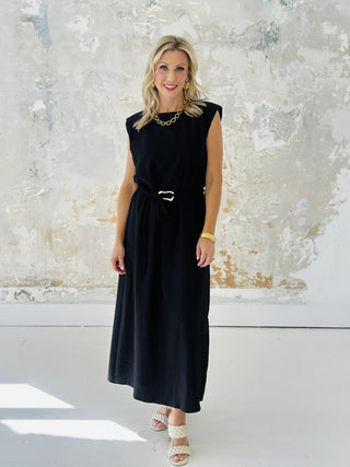 Woman wearing Miley Black Dress, sleeveless black midi dress with gold belt accent

Miley Black Dress with muscle shoulder design and slit hem

Black midi dress with gold embellished belt and back keyhole closure

Elegant sleeveless black dress styled with strappy heels