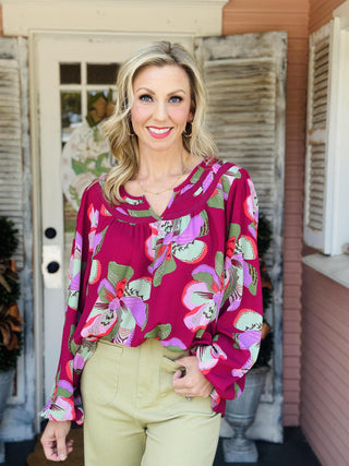 "Janelle Center Stage Plum Top with bold floral print and long sleeves"

"Plum blouse with oversized pink and green floral pattern and ruffle neckline"

"Women’s floral long sleeve top in plum with gathered neckline and relaxed fit"