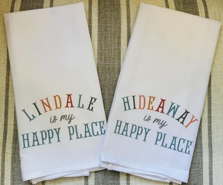 White cotton Happy Place tea towels available in Lindale or Hideaway designs with colorful typography.