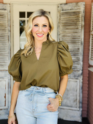 Woman wearing olive green ruffle v-neck top with puff sleeves

Olive green short sleeve blouse with textured fabric and gathered shoulders

Emory Top with puffed sleeves and ruffled neckline in textured olive fabric