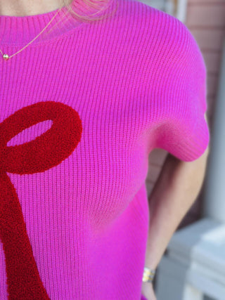 Bright pink knit Lilah Top with red bow detail on front, short sleeves

Women’s pink sweater top with textured red bow design, casual chic style

Close-up of pink knit Lilah Top fabric with raised red bow applique

Short sleeve pink knit top with bold red bow graphic, women’s fashion

Lilah Top pink sweater styled with jeans for everyday wear