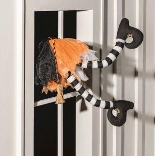 Crashing Witch Legs Halloween decoration with black and white striped stuffed legs, orange, black, and white tulle tutu, raffia broom, and suction cups for windows or doors.