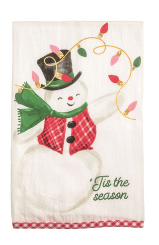 Cream cotton Christmas hand towel featuring a whimsical snowman with a plaid scarf, top hat, colorful Christmas lights, "'Tis the Season" sentiment, and a red gingham hem.